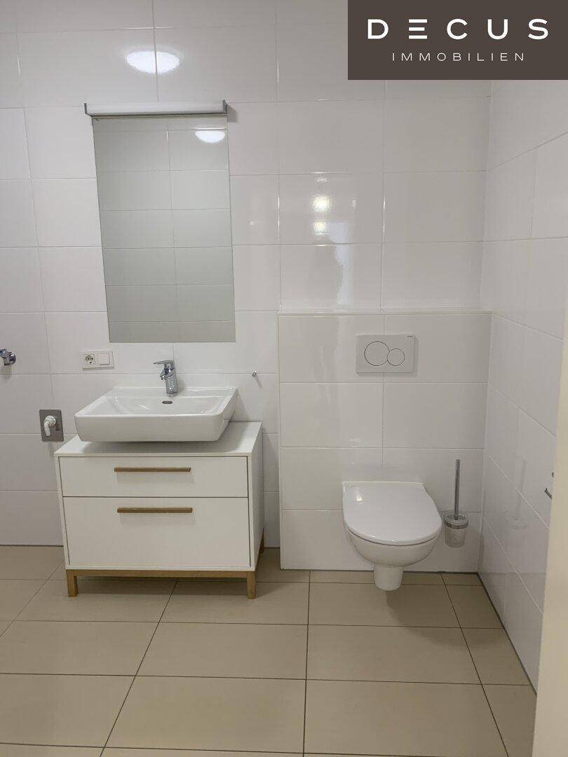 Modernes Gäste-WC mit weißen Fliesen, wandhängendem WC und einem stilvollen Waschbecken.