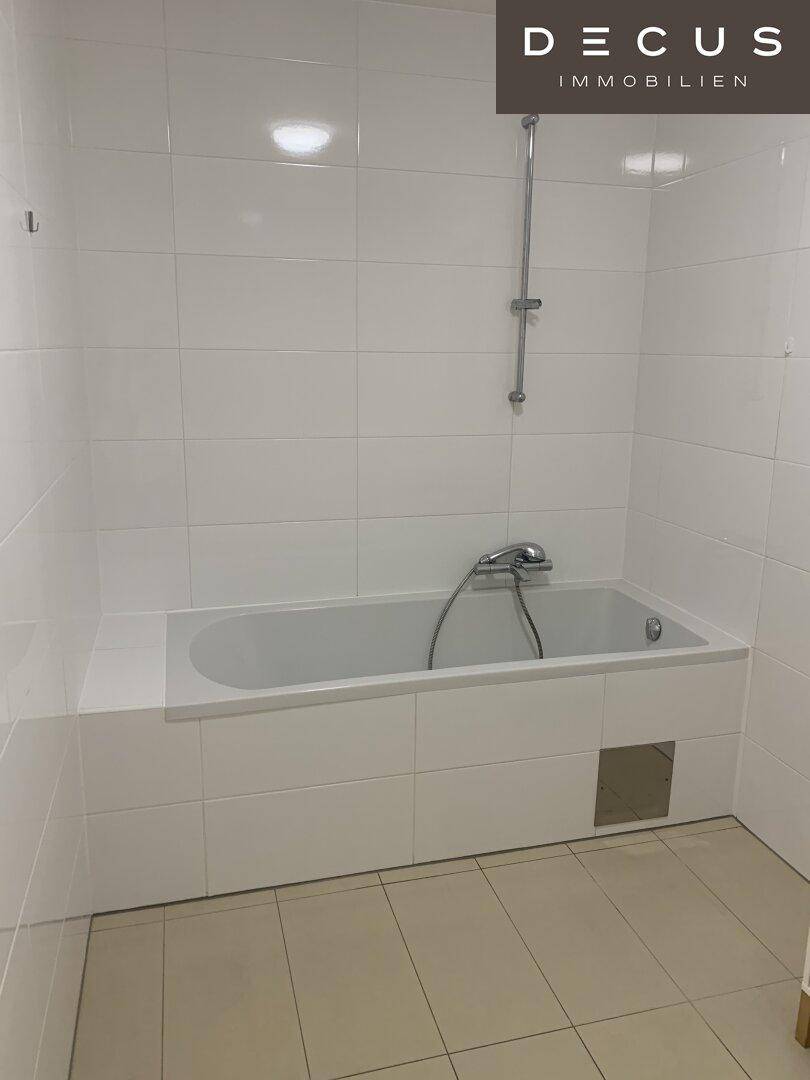 Helles Badezimmer mit weißen Wandfliesen und einer eingebauten Badewanne.