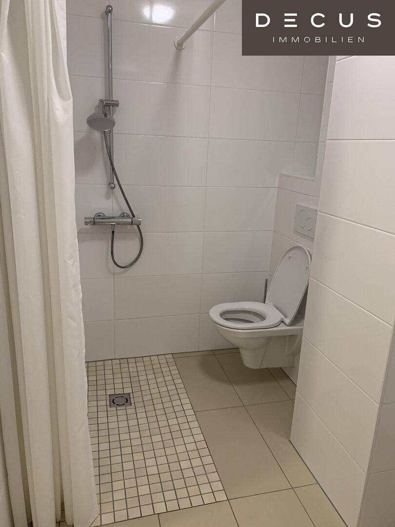 Modernes Badezimmer mit ebenerdiger Dusche, weißen Fliesen und wandhängendem WC.