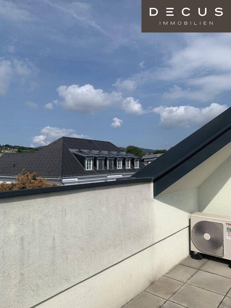 Dachterrasse mit Fliesenboden und Blick auf die umliegenden Dächer und den Himmel.