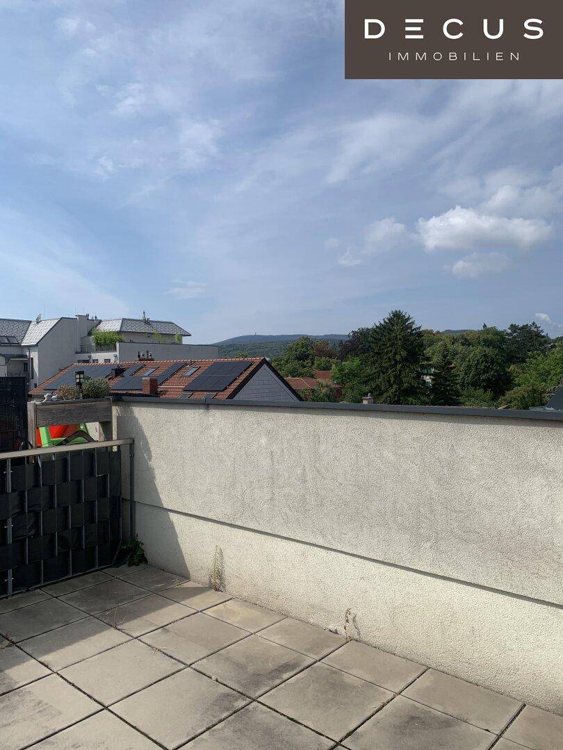 Geräumige Dachterrasse mit Fliesenboden und weitem Blick über die Dächer und grüne Hügel.