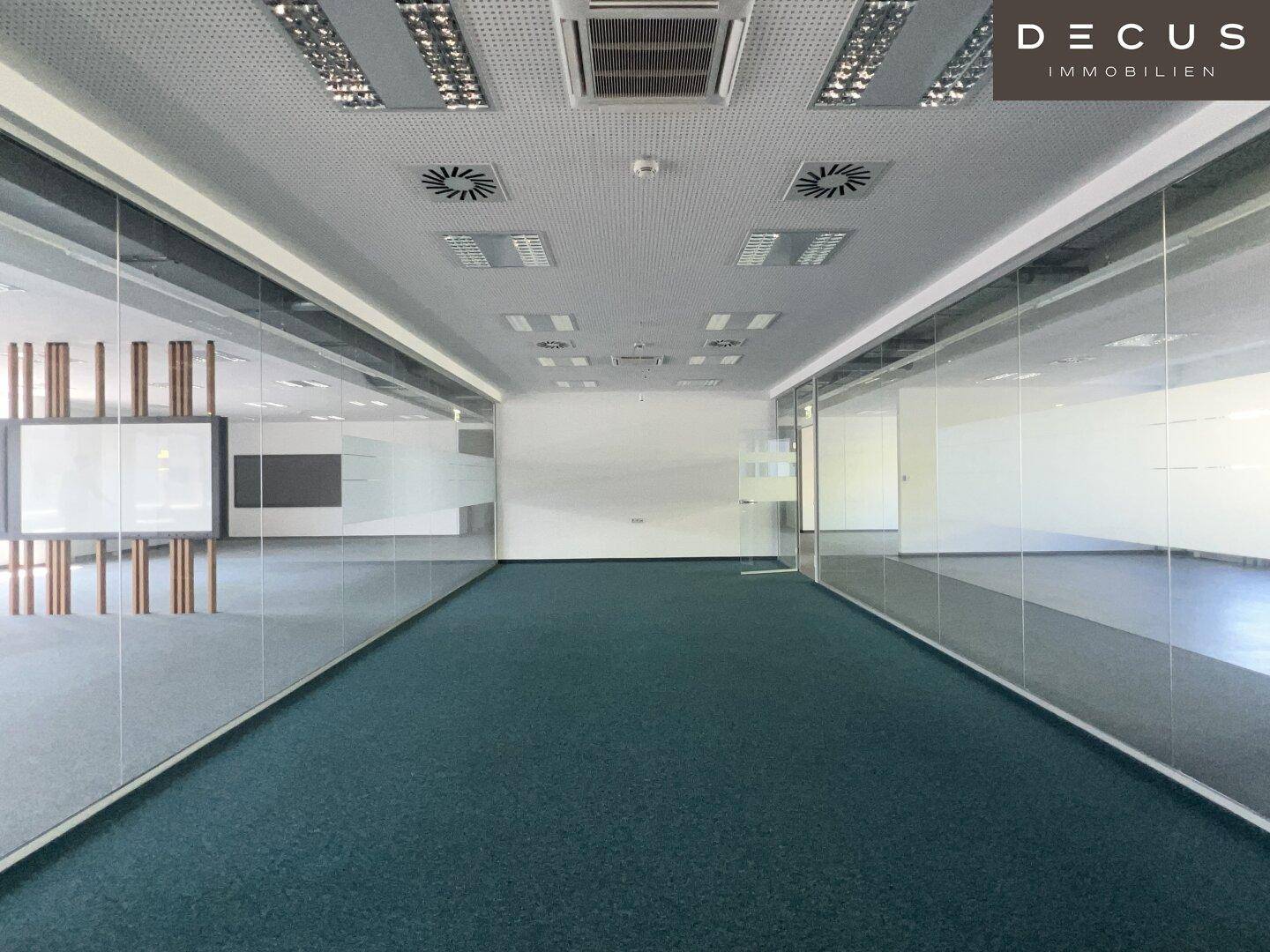Weitläufiger Bürobereich mit Teppichboden, Glaswänden und Deckenplatten mit integrierter Beleuchtung.