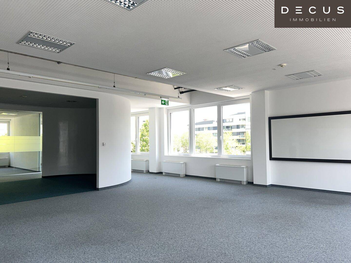 Geräumiger Bürobereich mit Teppichboden, großen Fenstern und einer runden Säule im Vordergrund.
