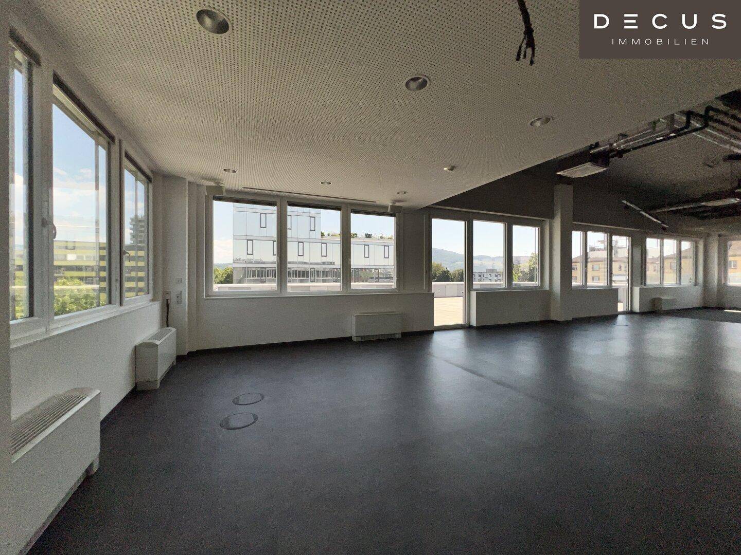 Heller Büroraum mit dunklem Boden und einer Reihe von Fenstern, die einen weiten Blick bieten.