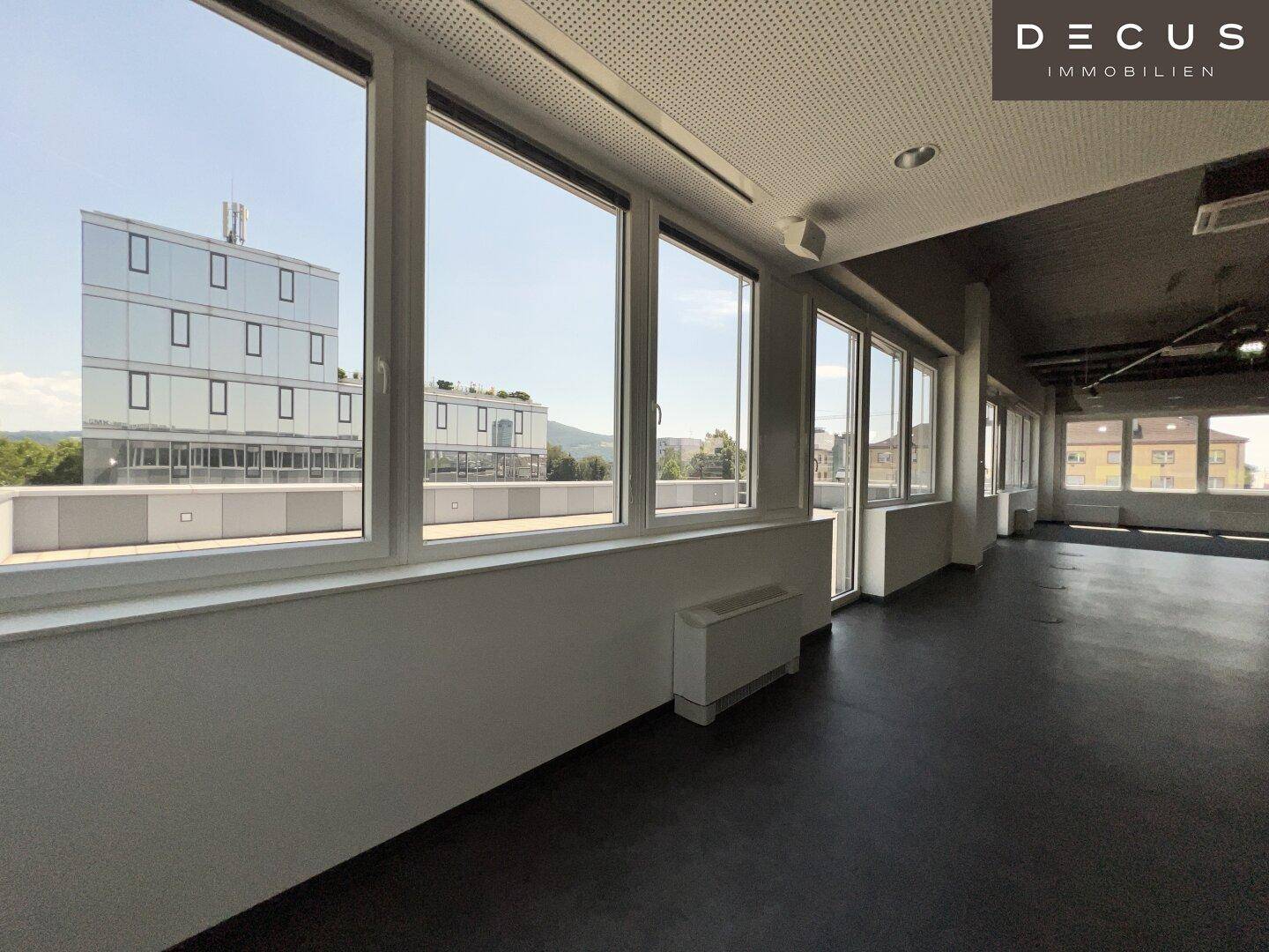 Moderner Büroraum mit großen Fenstern, die einen Blick auf die umliegenden Gebäude und die Stadt ermöglichen.