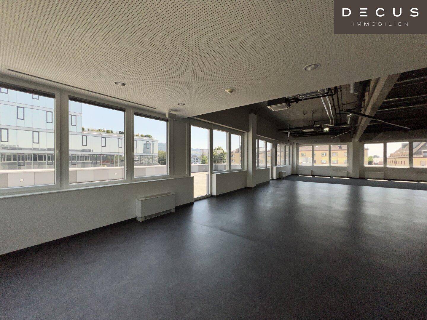Geräumiger Bürobereich mit dunklem Boden und vielen Fenstern, die für eine helle und offene Atmosphäre sorgen.