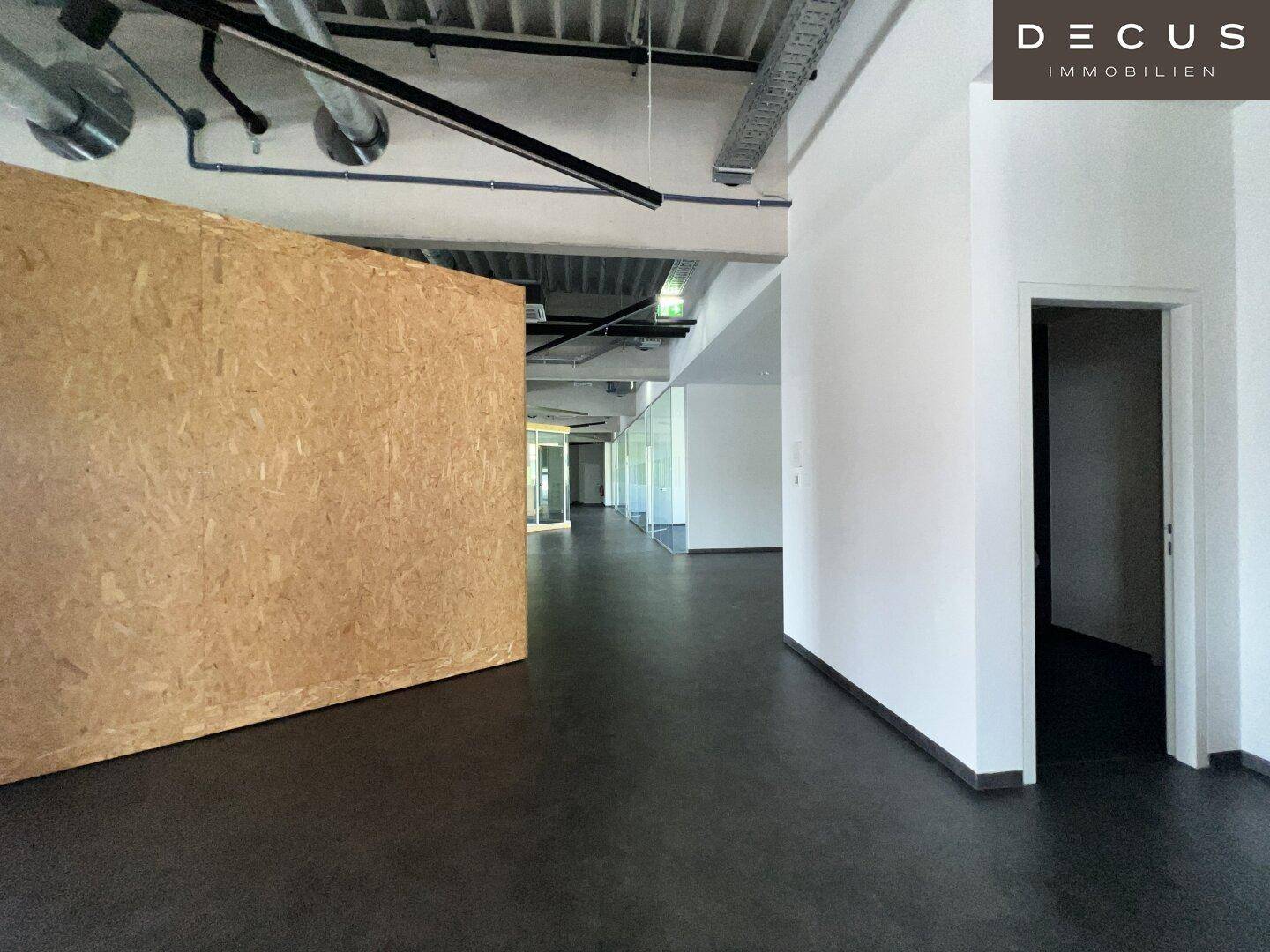 Langer Flur in einem Bürogebäude mit freiliegenden Lüftungsrohren und einer Wand aus OSB-Platten.