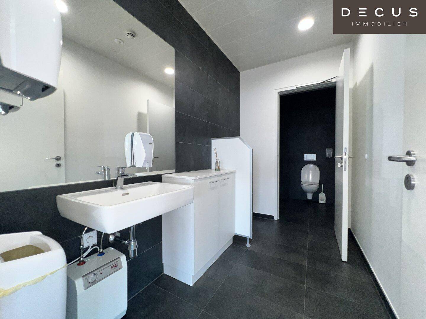 Modernes Badezimmer mit großem Spiegel, Waschbecken und dunklen Fliesen an Wand und Boden.