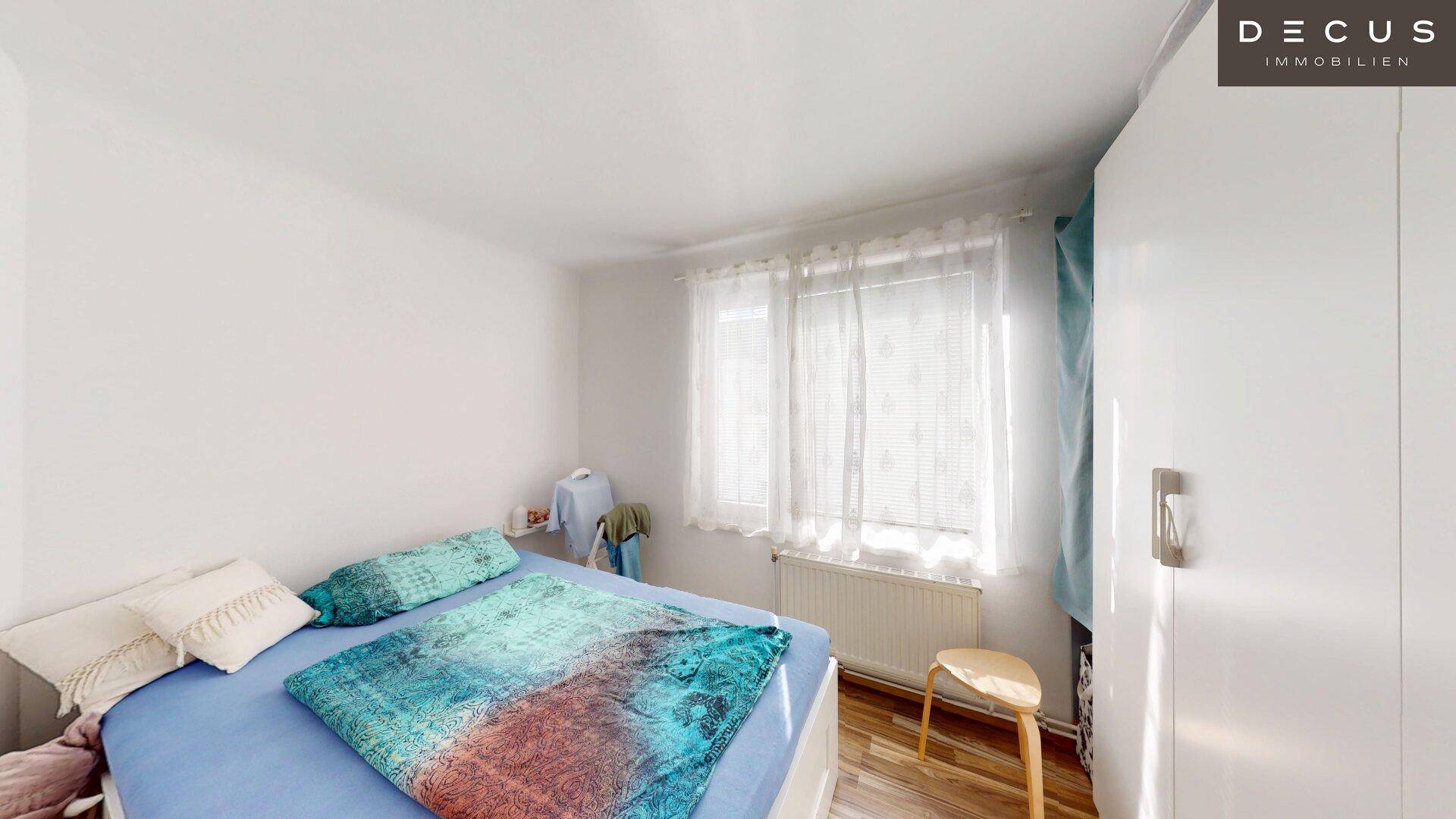 Schlafzimmer mit hellem Fenster, bequemen Bett und einem Heizkörper unter dem Fenster.
