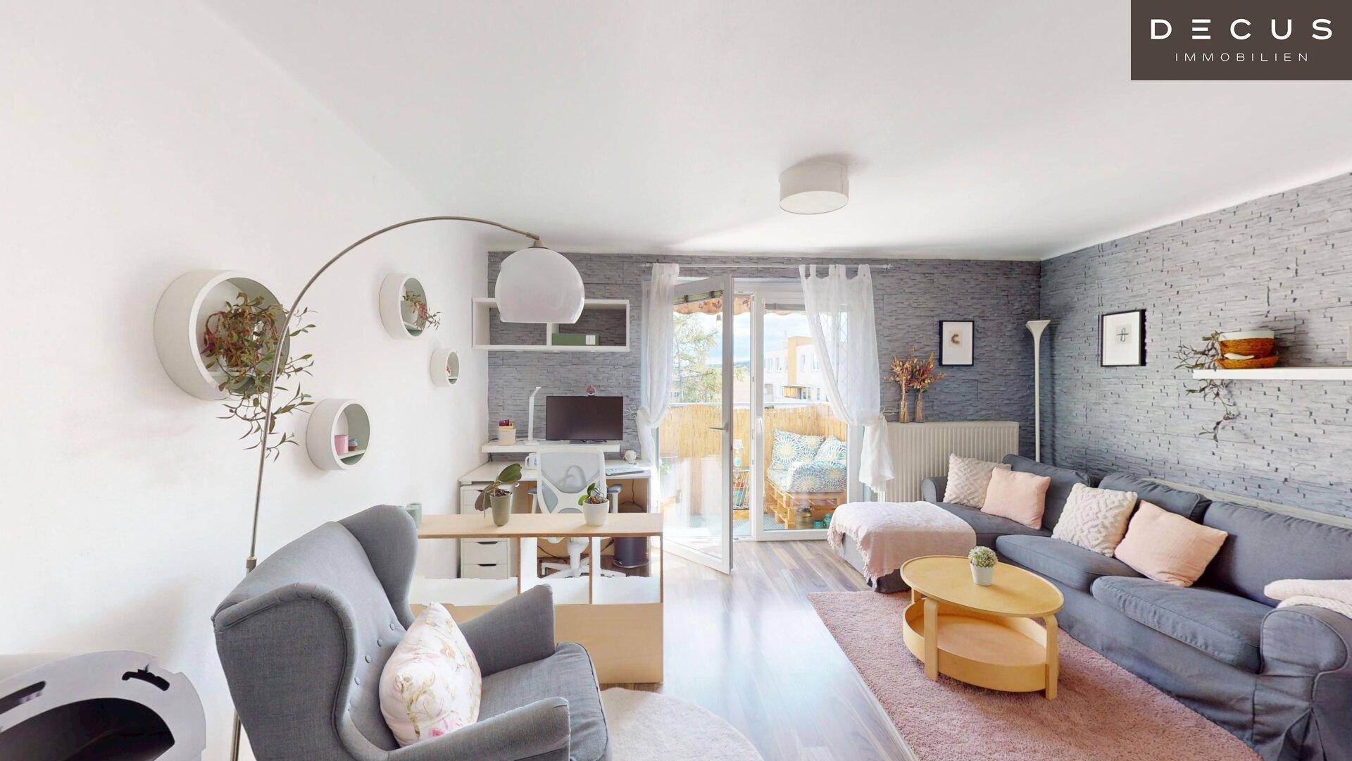 Geräumiges Wohnzimmer mit Sofa, Sessel, Arbeitsplatz und Zugang zum sonnigen Balkon.