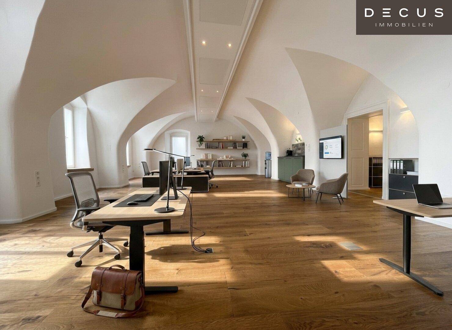 Modern eingerichteter Bürobereich mit Gewölbedecken, Holzboden und viel Tageslicht, ideal für kreatives Arbeiten.