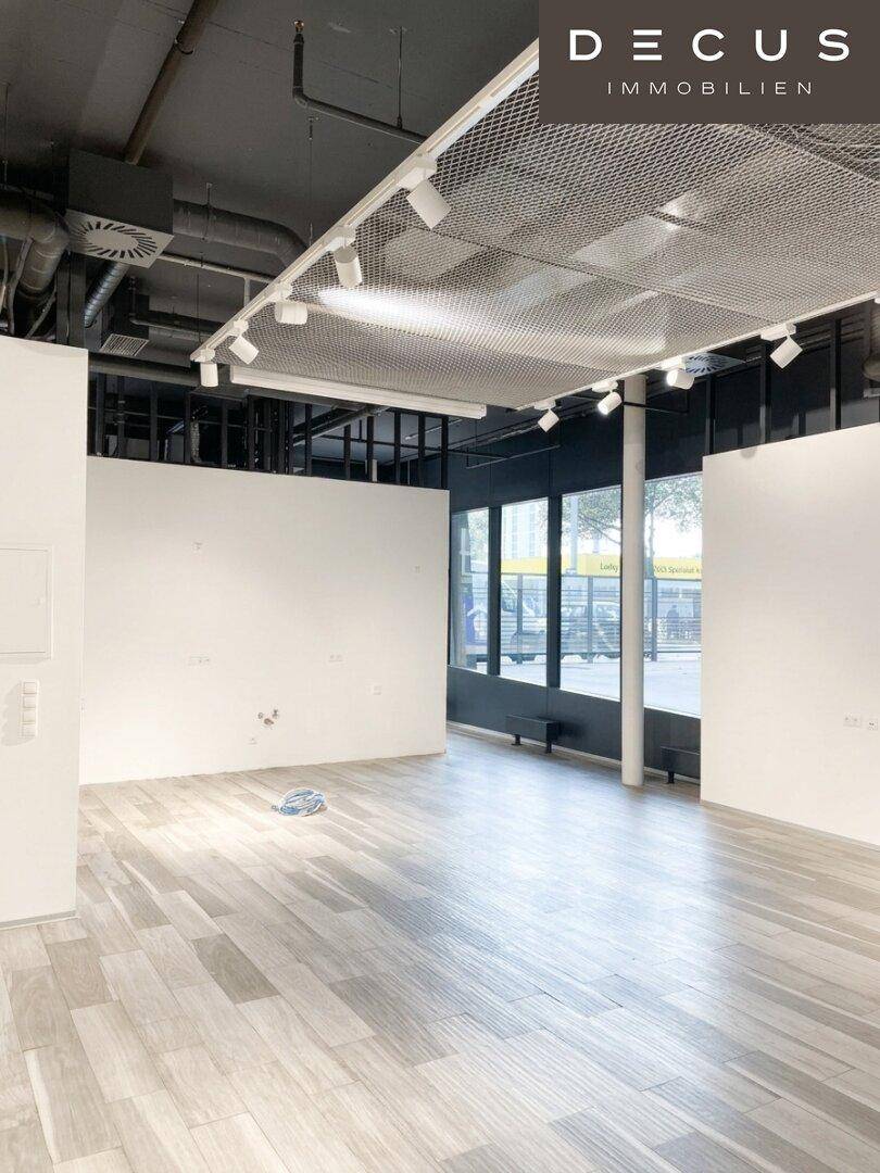 Heller, leerer Gewerberaum mit modernen Deckenleuchten, großen Fenstern und Holzboden.