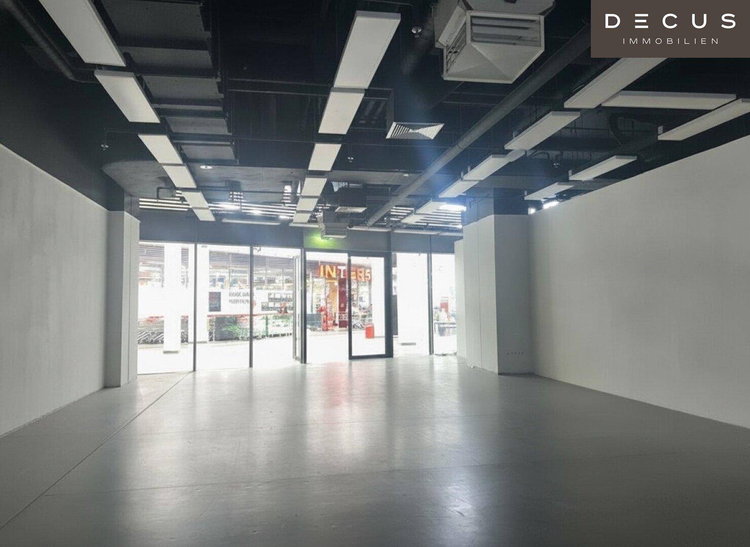 Heller Gewerberaum mit Blick auf die Eingangstüren des Einkaufszentrums und sichtbaren Deckeninstallationen.