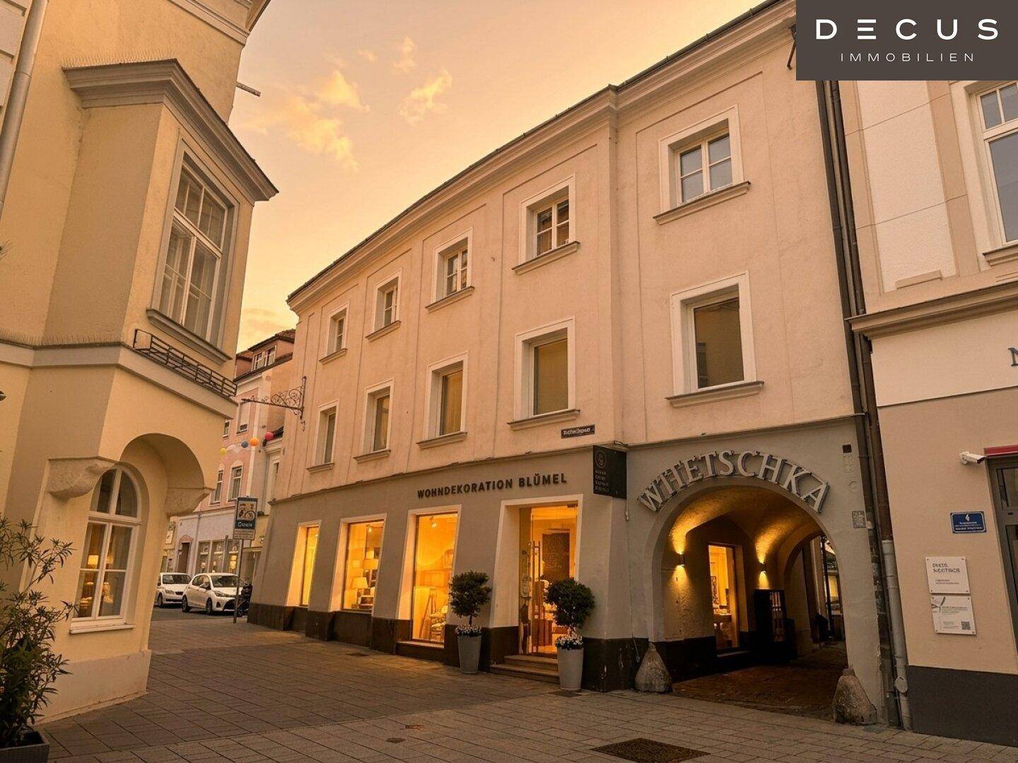 Historisches Gebäude mit Ladenfront und Wohnungen, beleuchtet bei Sonnenuntergang.