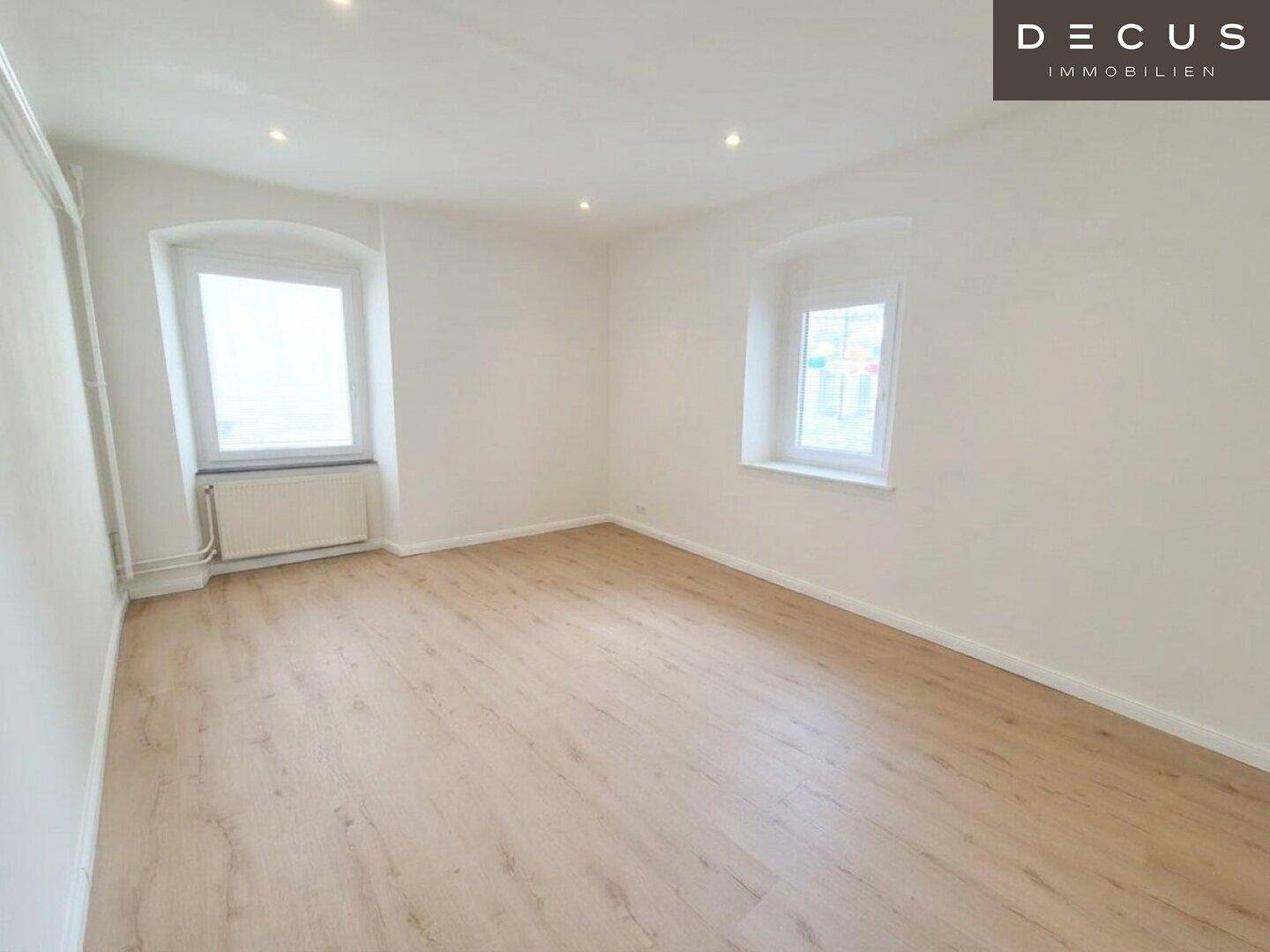 Helles Schlafzimmer mit Laminatboden, Einbaustrahlern und zwei Fenstern.
