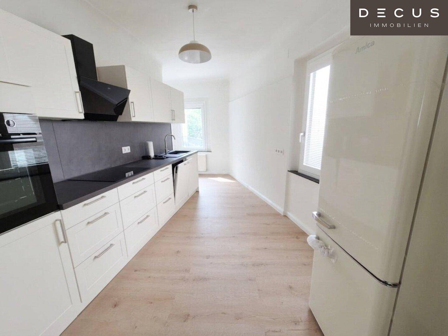 Moderne Einbauküche mit weißen Schränken, dunkler Arbeitsplatte und Kühlschrank.