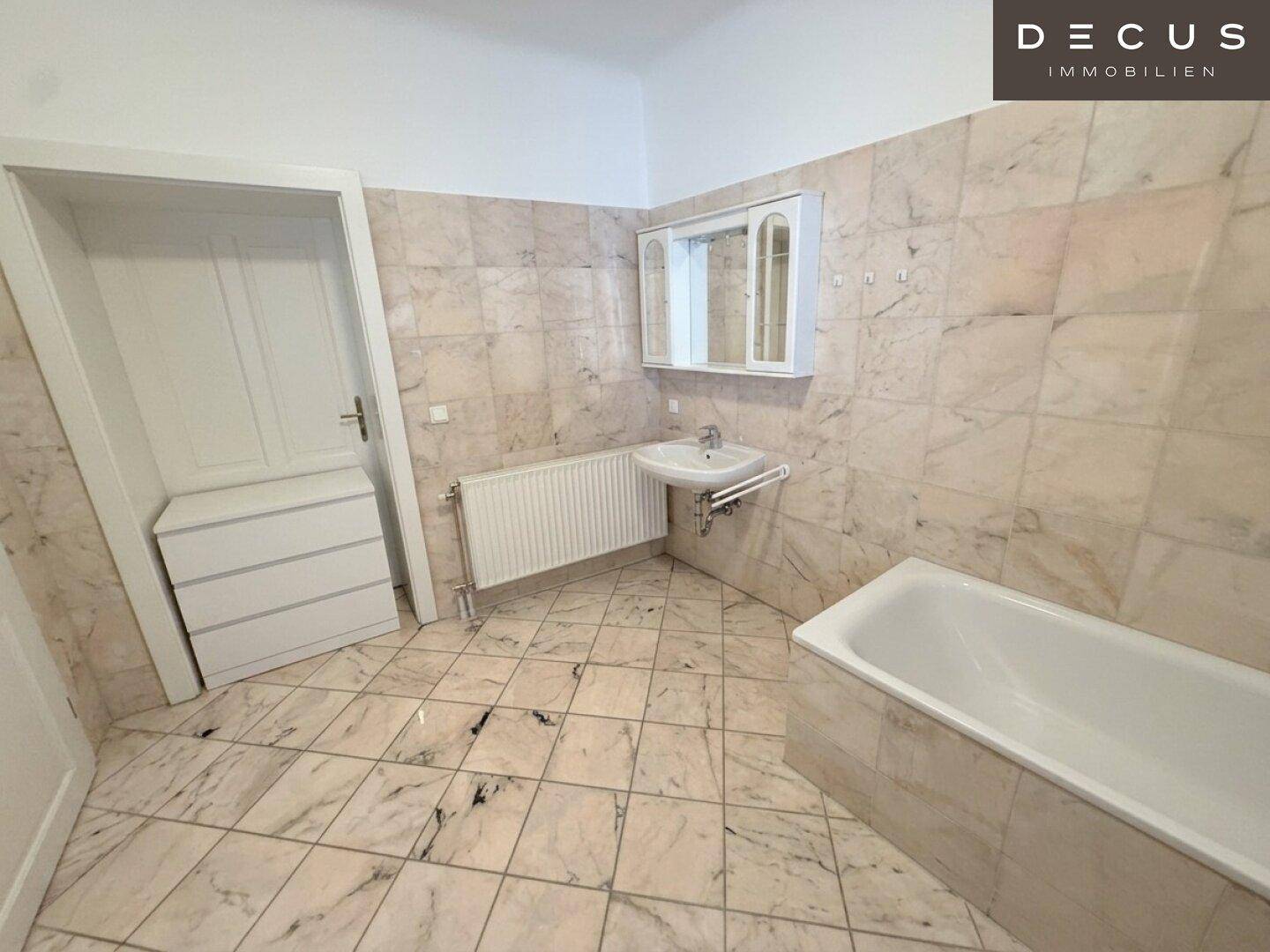 Badezimmer mit Marmorfliesen, Badewanne und Waschbecken mit Spiegelschrank.