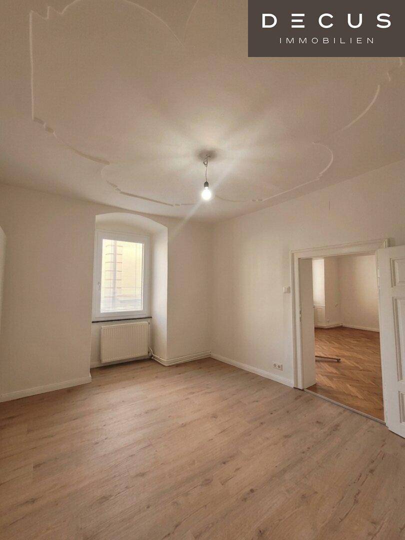 Schlafzimmer mit Laminatboden, einem Fenster und dekorativer Decke.