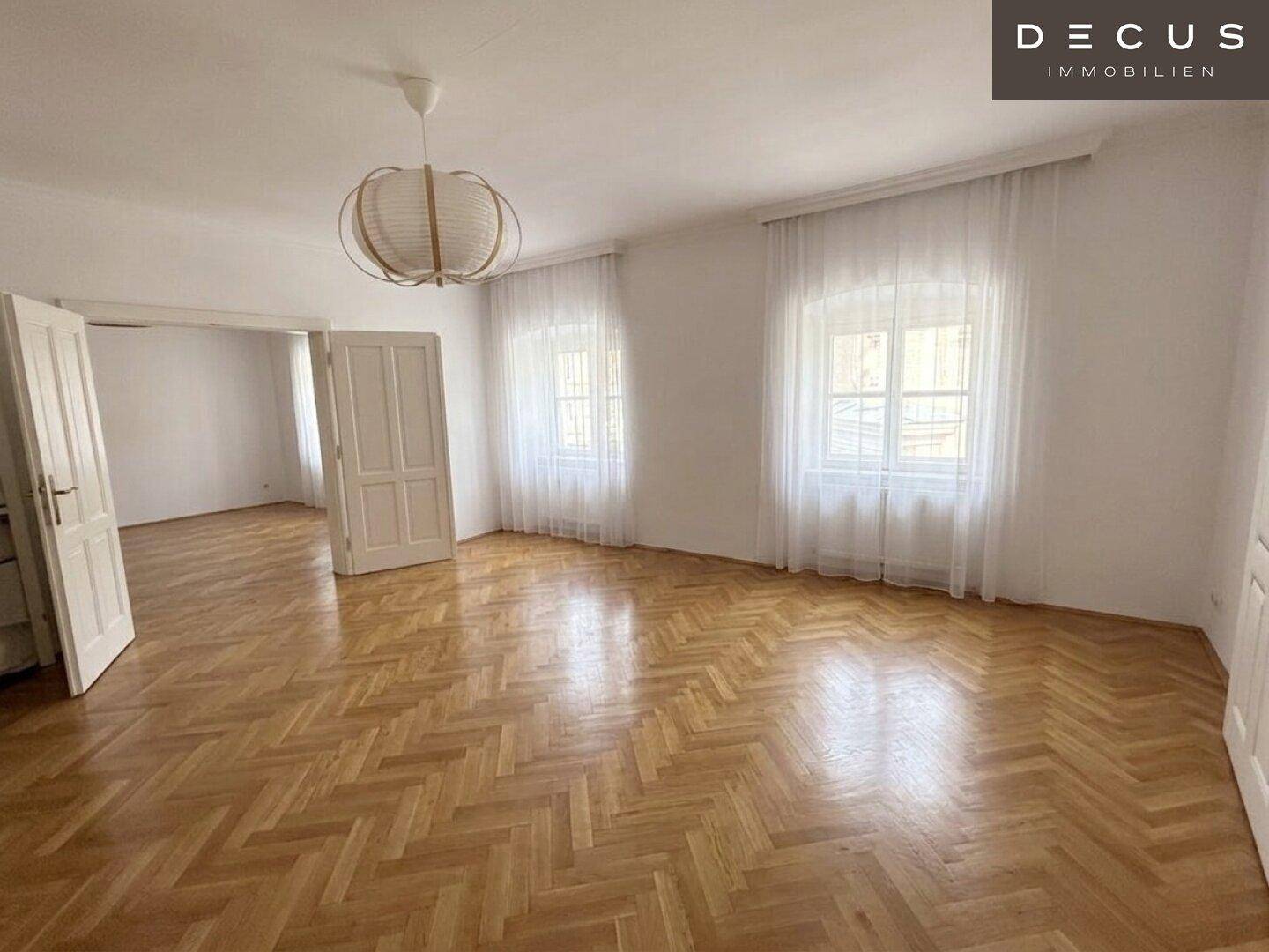 Helles Wohnzimmer mit Fischgrätparkett, großen Fenstern und leichter Vorhangdekoration.