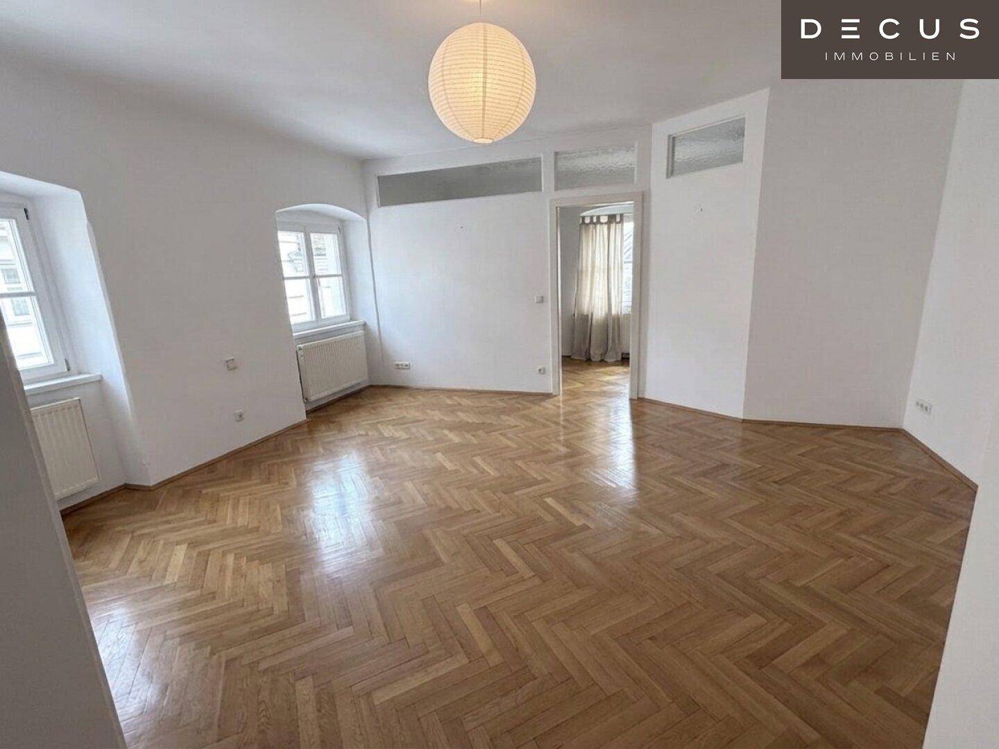 Geräumiges Wohnzimmer mit Fischgrätparkett und mehreren Fenstern, hell und einladend.