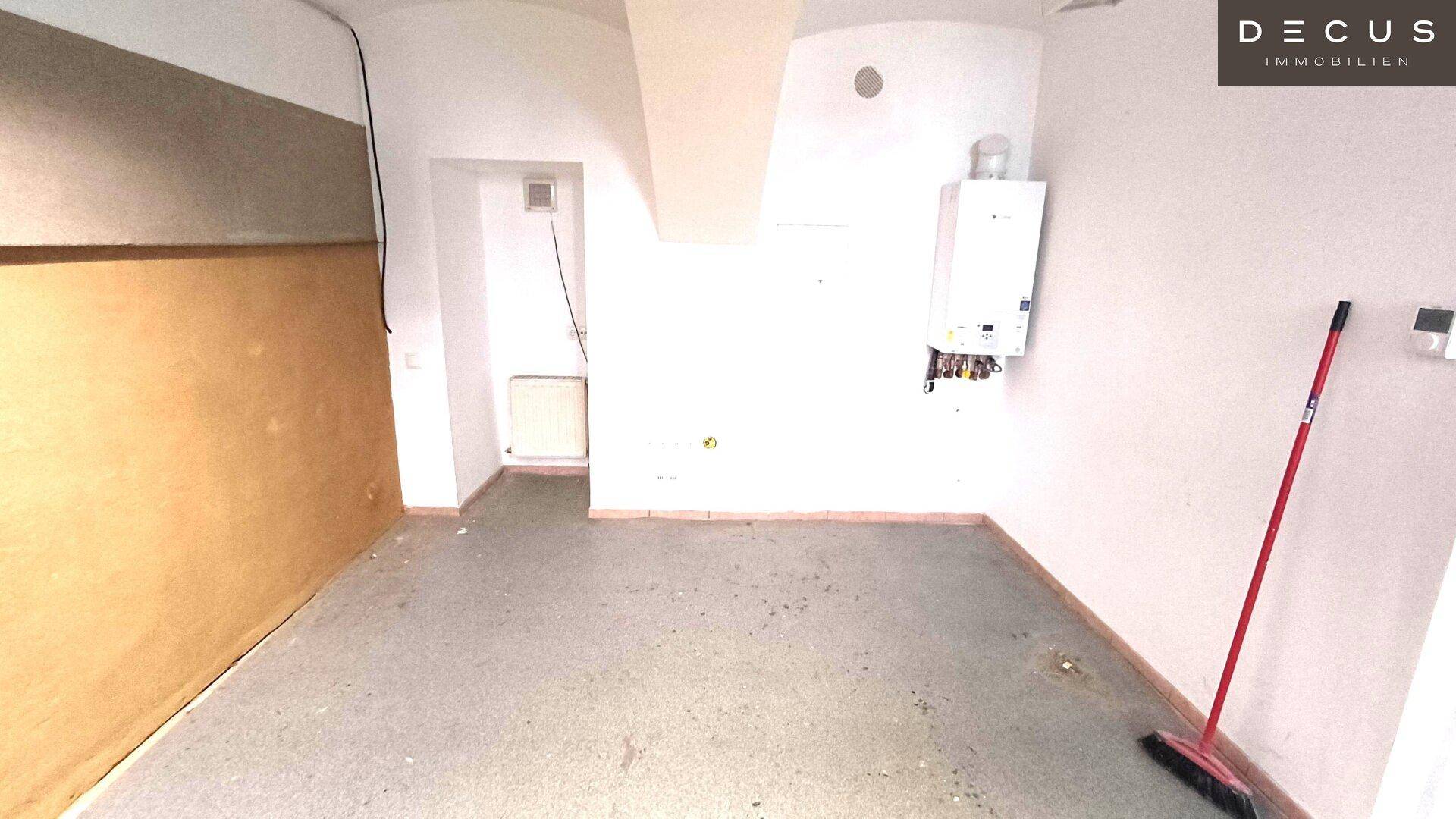 Einfacher Innenraum mit Boiler an der Wand und Betonboden, der als Abstellraum genutzt werden könnte.