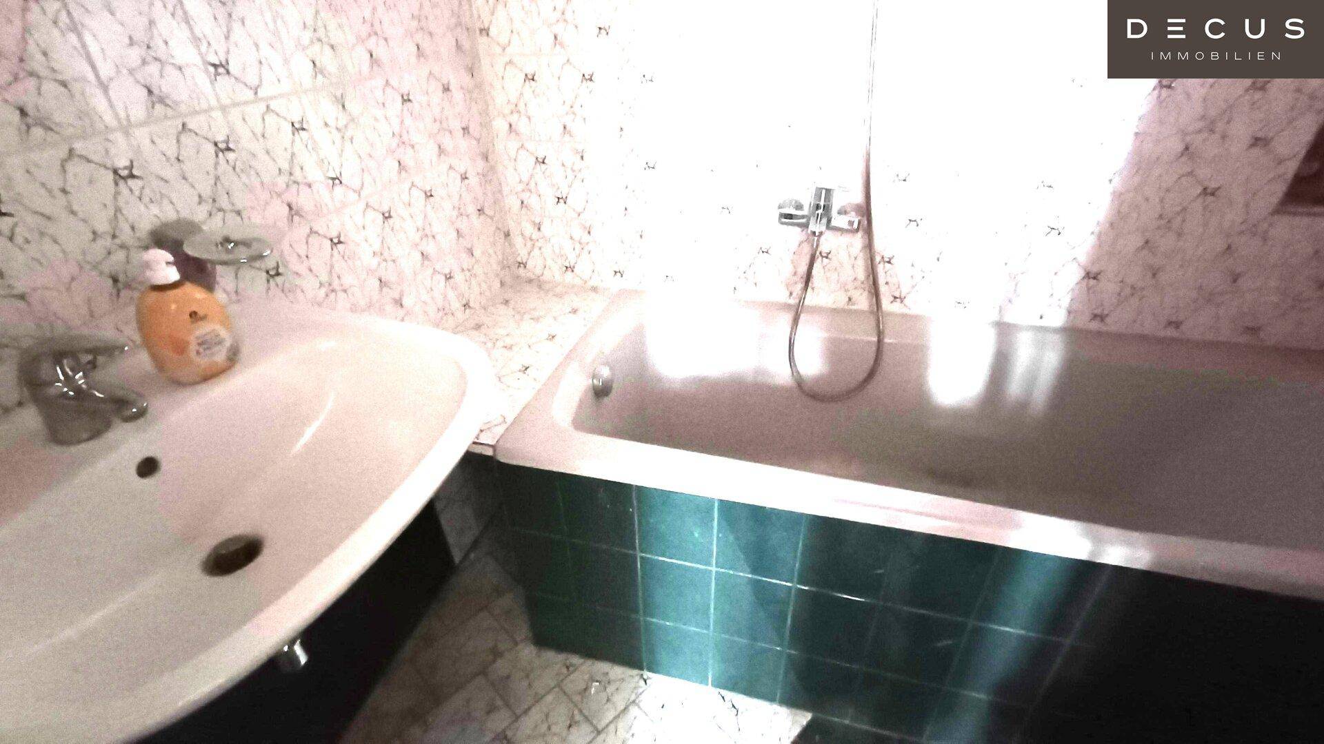 Badezimmer mit Badewanne und Waschbecken, gefliesten Wänden und Boden in einem älteren Stil.