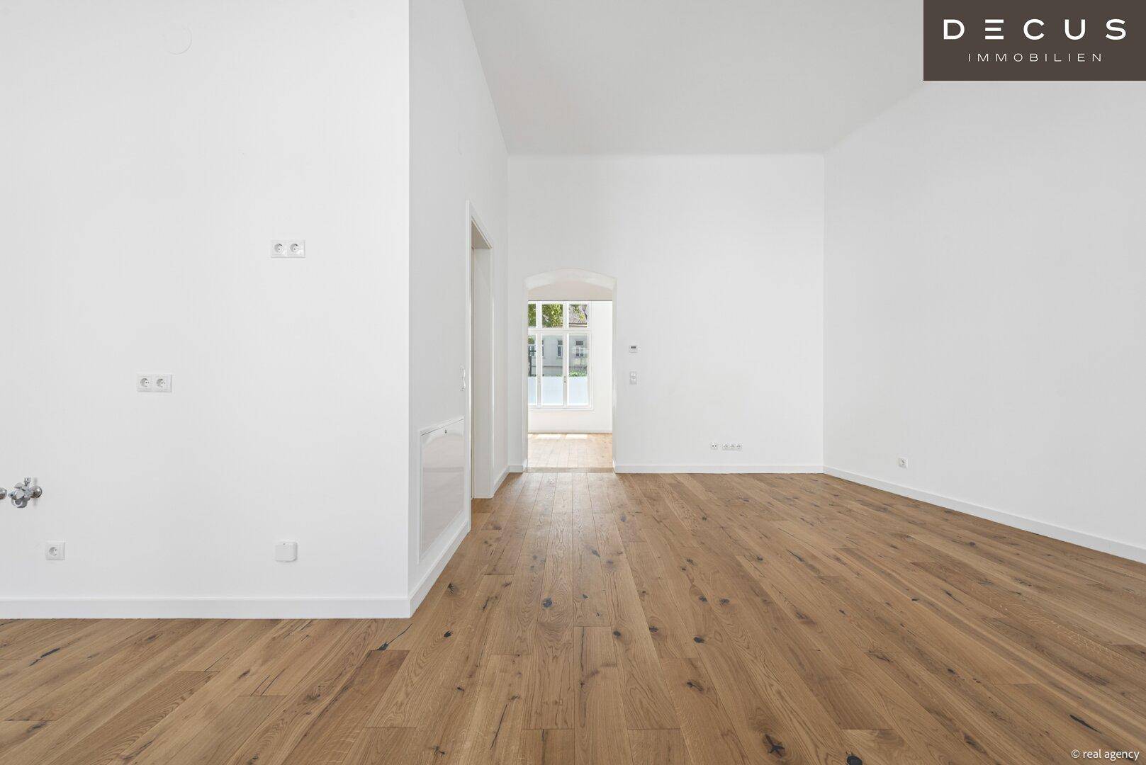 Geräumiger, heller Raum mit Holzboden und Durchgang zu weiteren Zimmern.