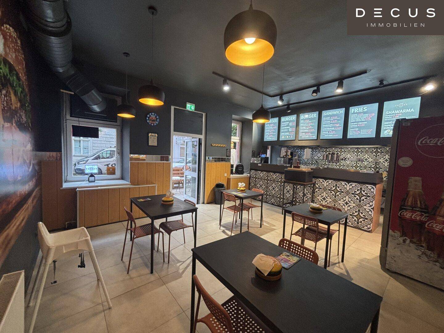 Blick in den Gastraum eines Restaurants mit Sitzgelegenheiten und Fenstern zur Straße.