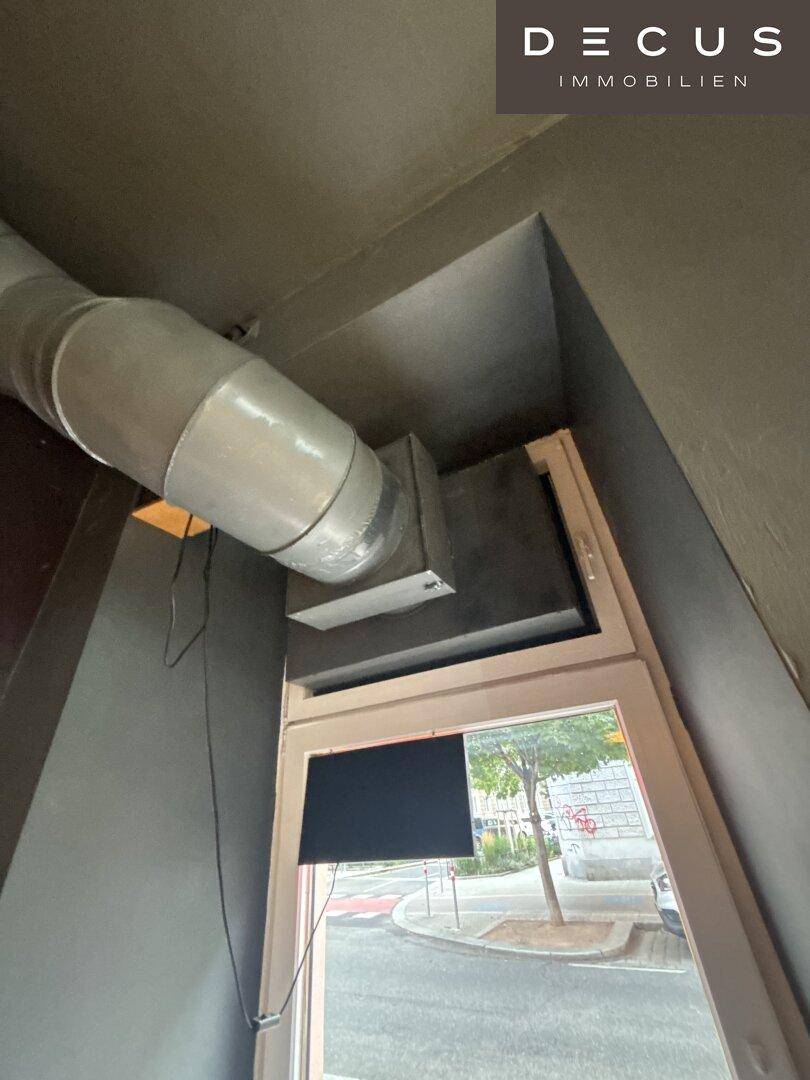 Detailaufnahme einer Lüftungsanlage und eines Fensters mit Blick auf die Straße.
