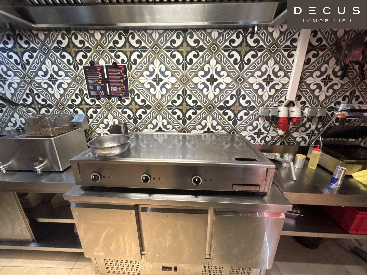 Kochbereich mit großer Grillplatte und Edelstahloberflächen in der Restaurantküche.