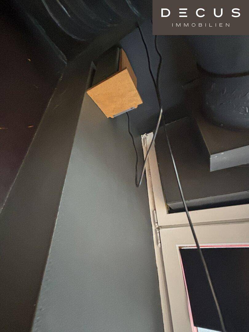 Detailaufnahme von Kabeln und einer Holzbox an der Decke über einem Fenster.