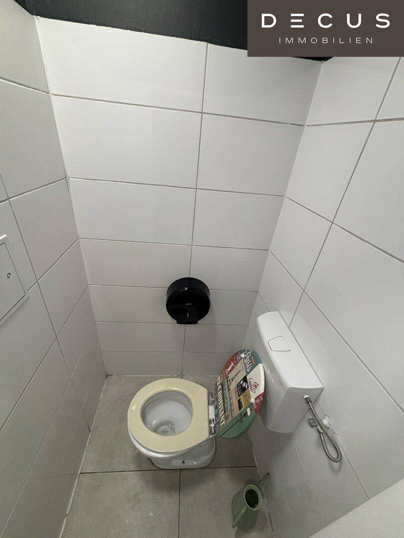 Kleine Toilette mit weißen Fliesen an den Wänden und einem einfachen WC.