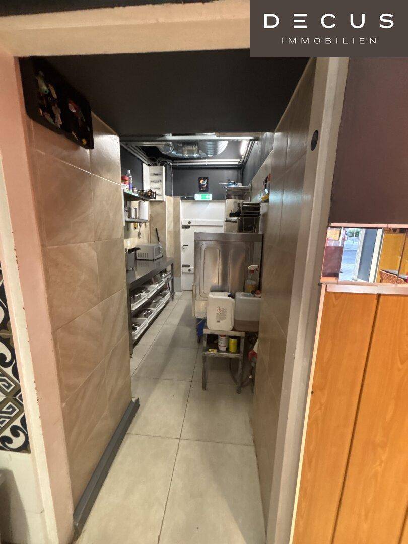 Schmaler Durchgang zu einem Küchenbereich mit gefliesten Wänden und sichtbaren Installationen, funktional gestaltet.
