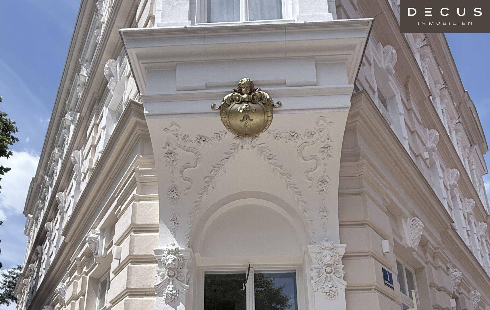 Detailaufnahme einer reich verzierten Gebäudeecke mit barocken Ornamenten und goldener Plakette.