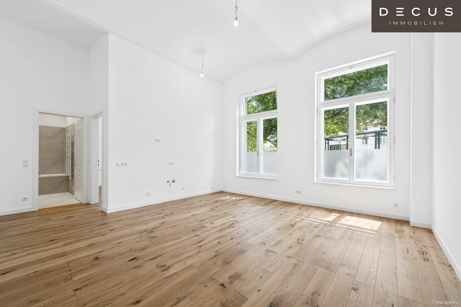 Helles Wohnzimmer mit Holzboden, hohen Fenstern und Blick ins Grüne.