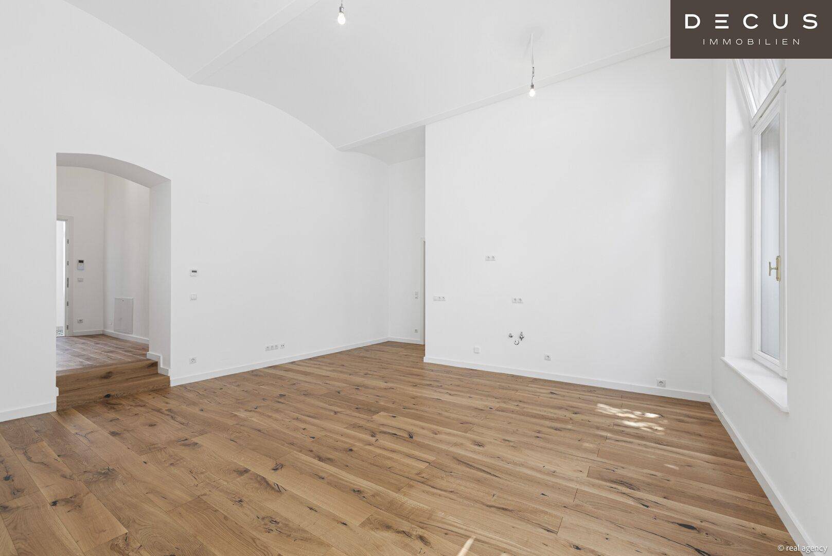 Geräumiges Wohnzimmer mit neuem Holzboden, hohen Decken und weiß gestrichenen Wänden.