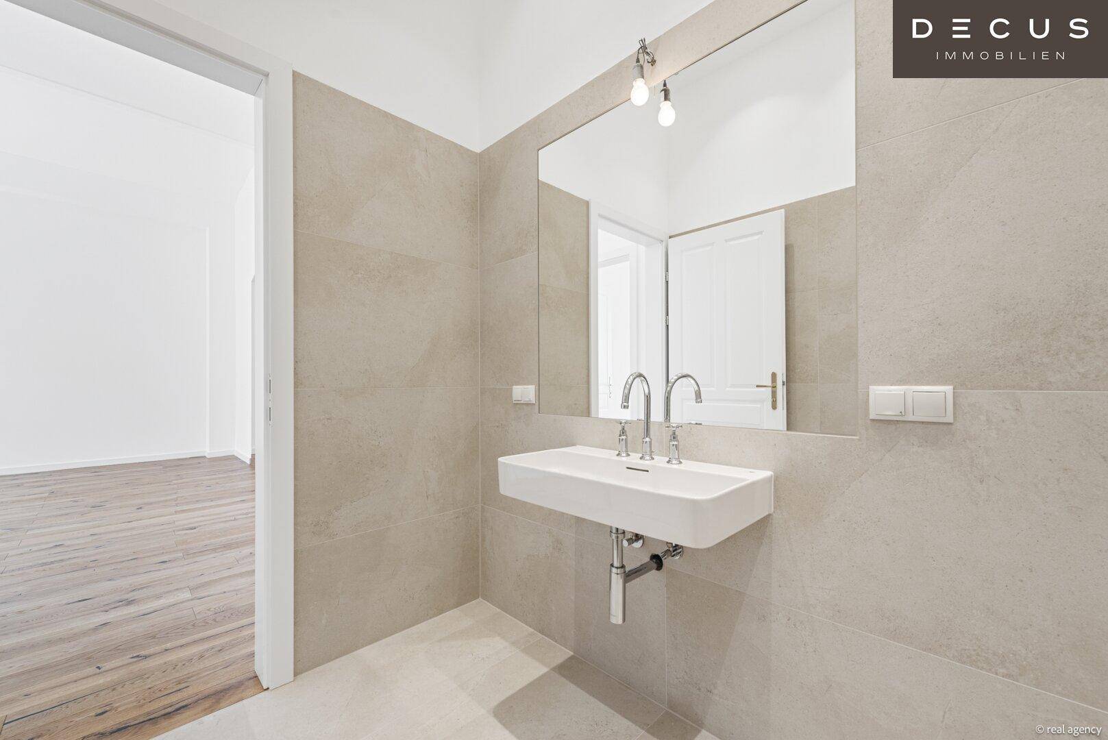 Elegantes Badezimmer mit modernem Waschtisch, großem Spiegel und hellen Fliesen.
