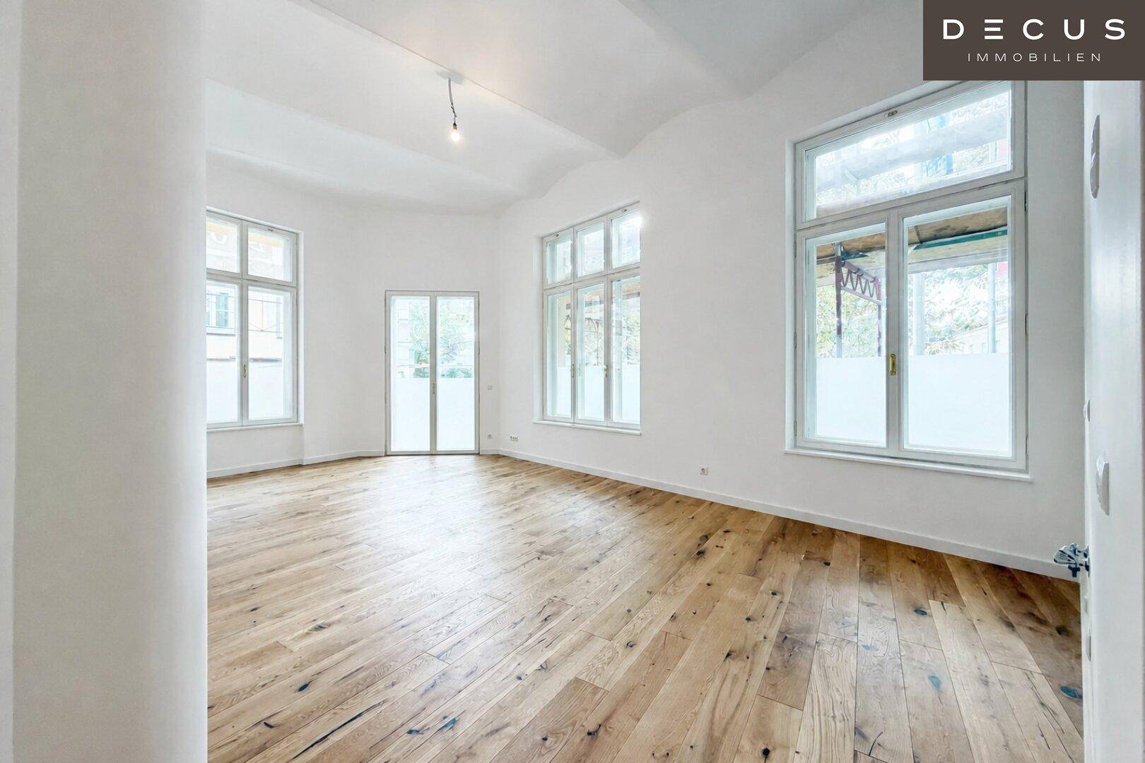 Geräumiger, heller Raum mit Holzboden und vielen Fenstern, die viel Tageslicht hereinlassen.