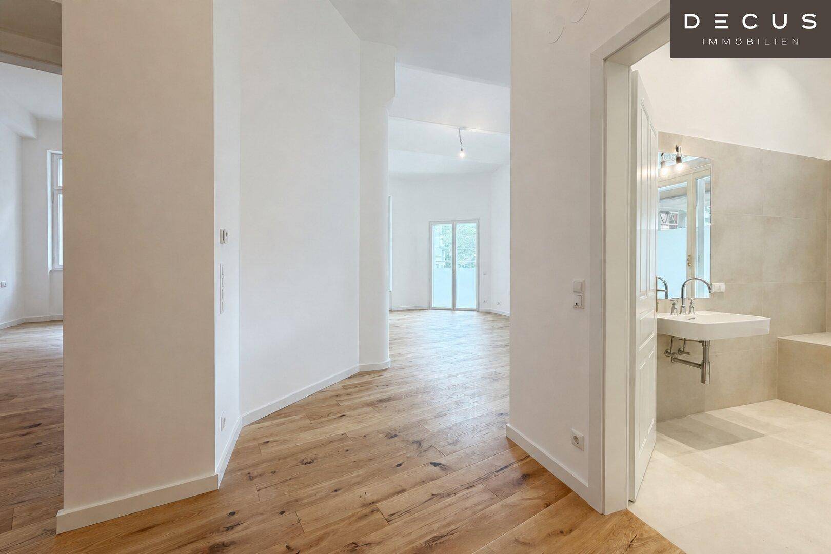 Heller Flur mit Holzboden, der zu einem weiteren Raum und einem modernen Badezimmer führt.