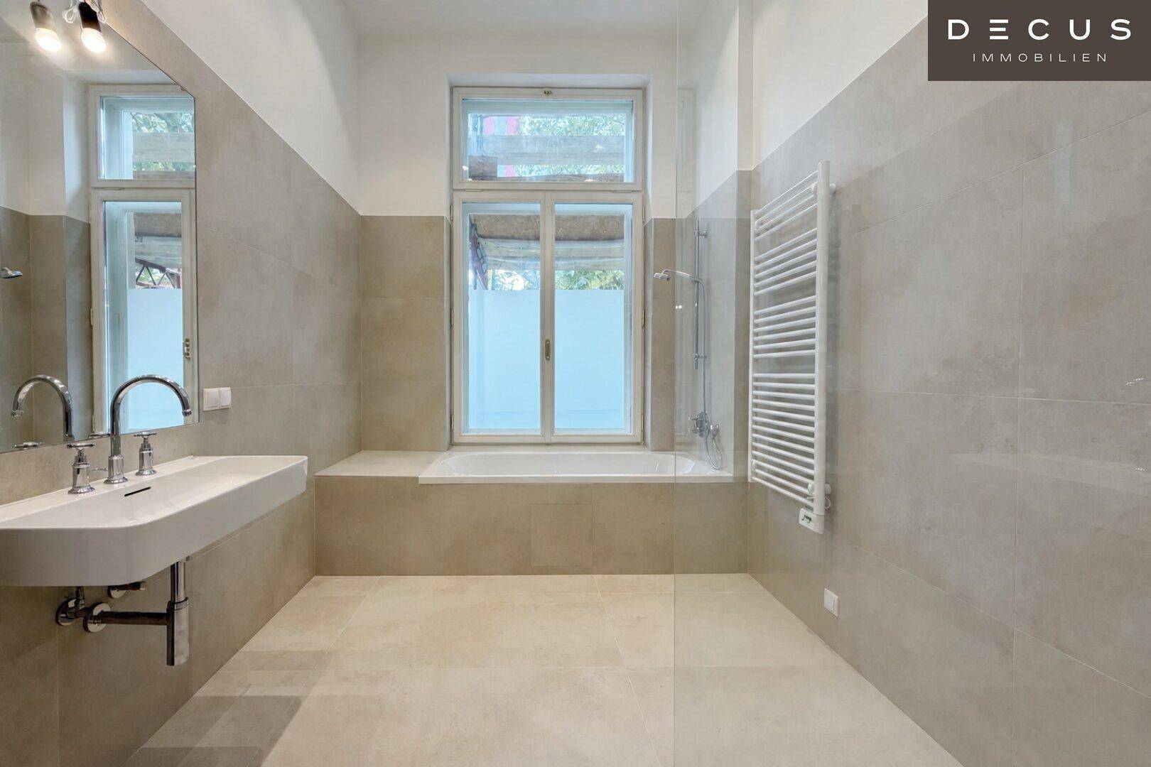 Modernes Badezimmer mit hellgrauen Fliesen, Badewanne, Einzelwaschbecken und Fenster.