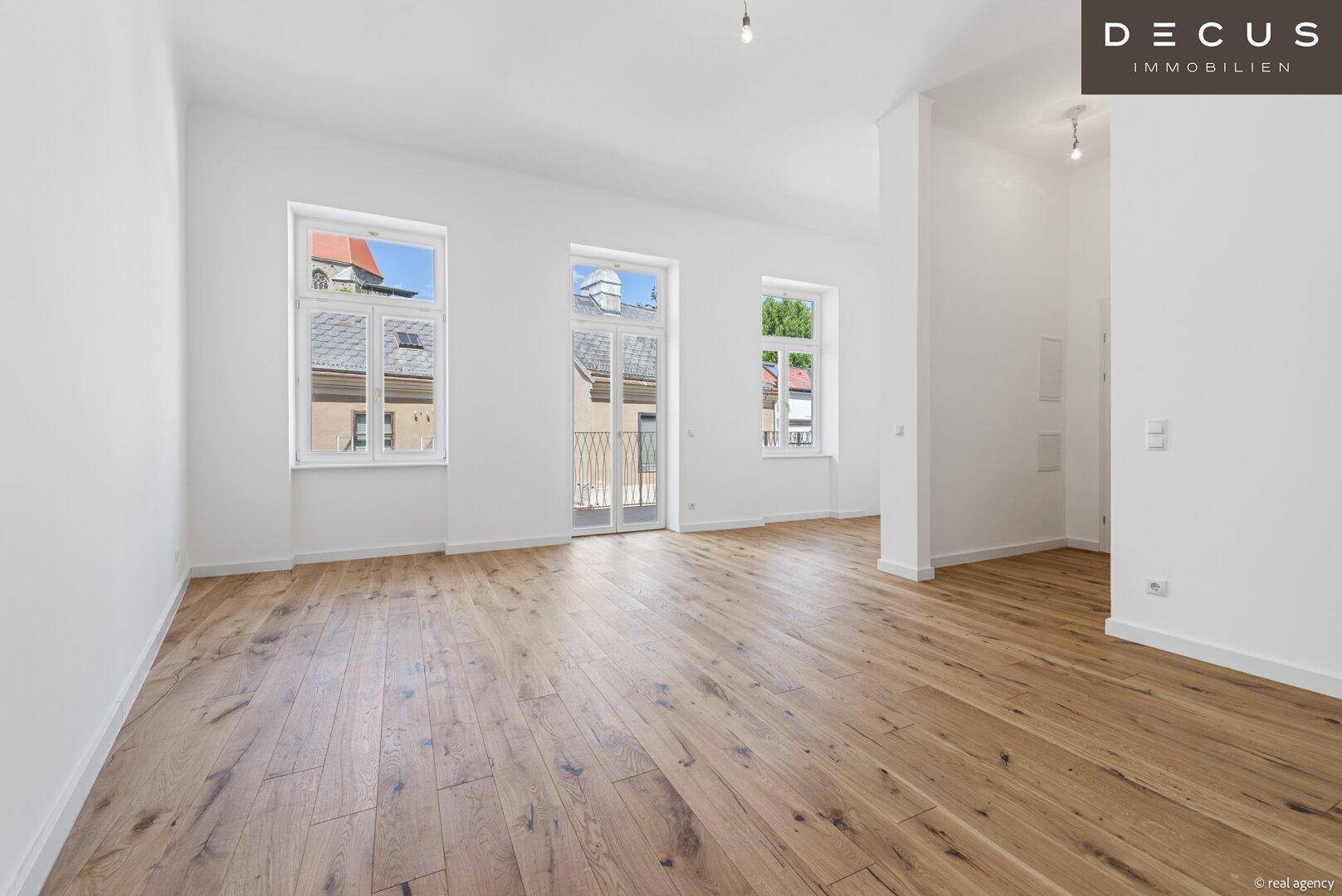 Heller, leerer Raum mit elegantem Holzparkett, hohen Decken und großen Fenstern mit französischem Balkon.