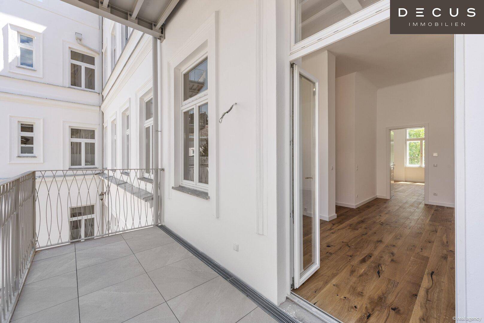 Geräumiger Balkon mit Fliesenboden und Blick auf den Innenhof, zugänglich vom Wohnbereich.
