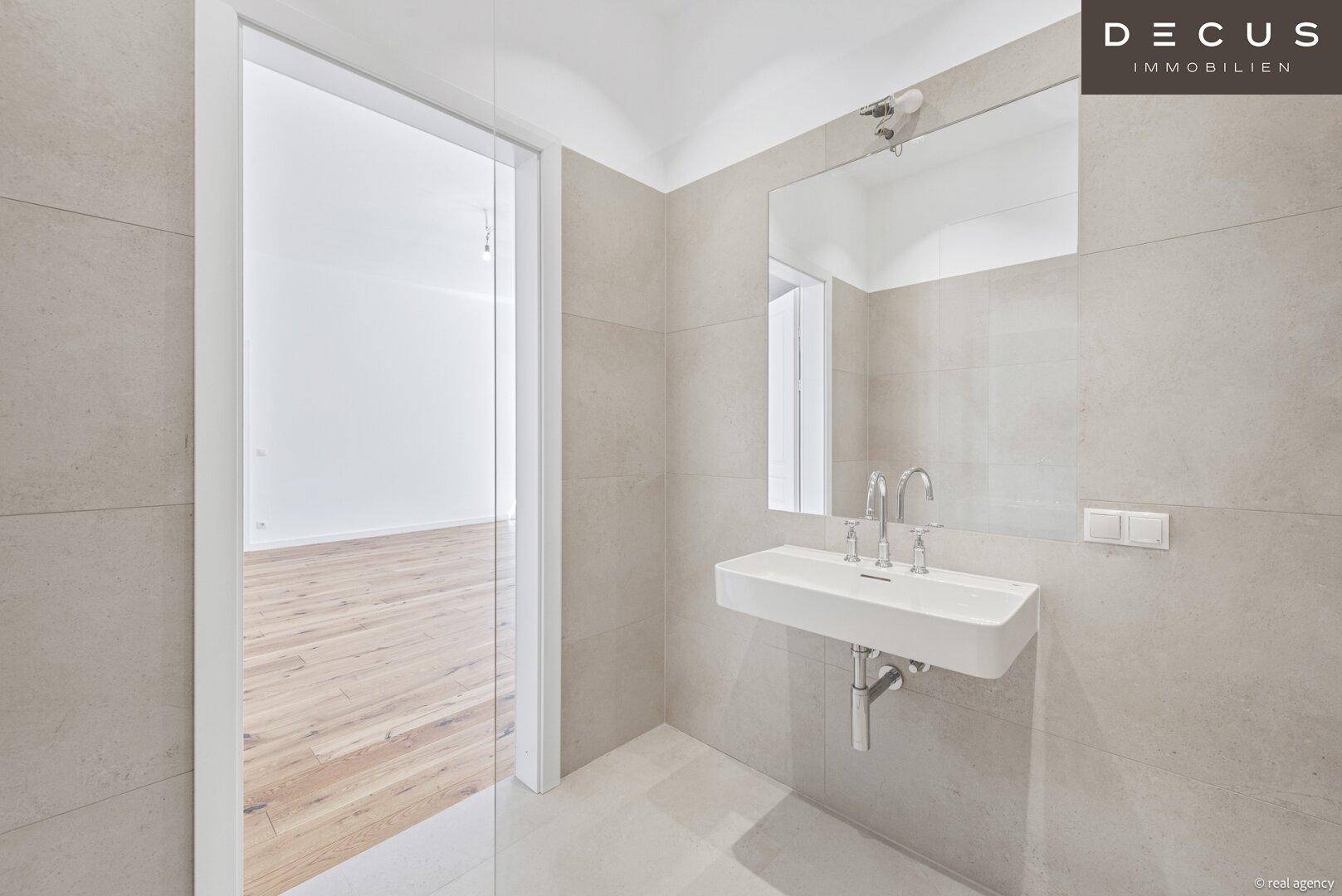 Modernes Badezimmer mit Waschbecken, großem Spiegel und Zugang zu einem weiteren Raum.