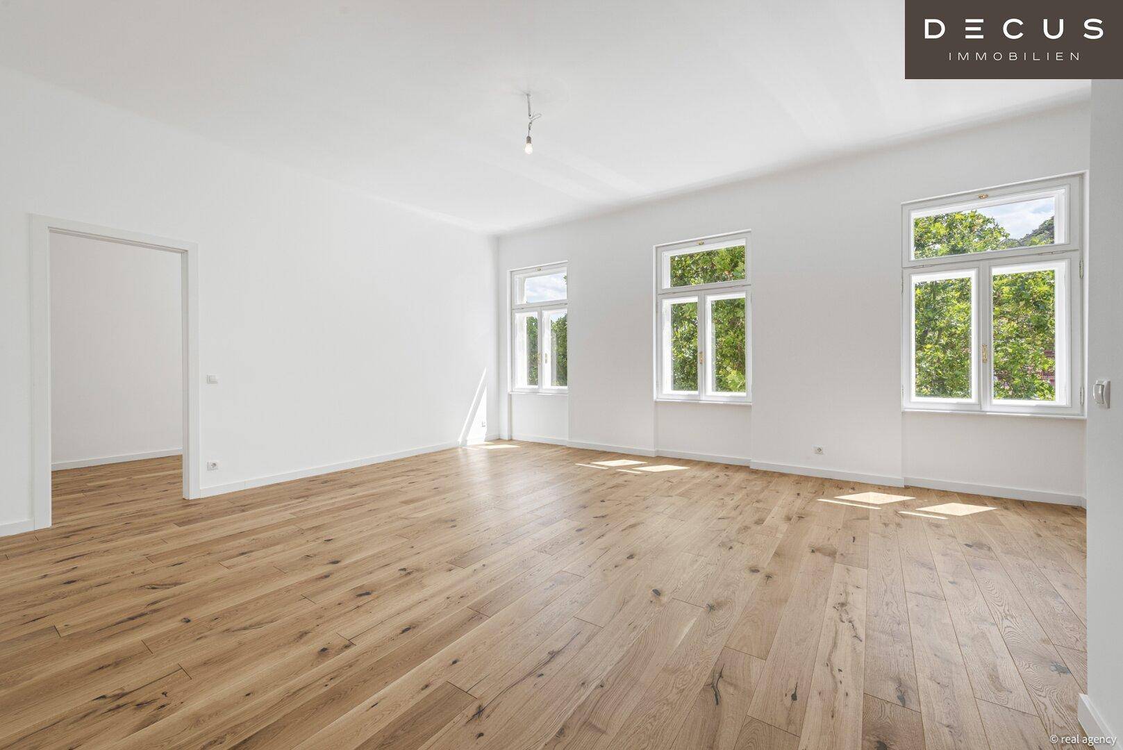 Geräumiger, heller Raum mit neu verlegtem Eichenparkett und großen Fenstern mit Grünblick.