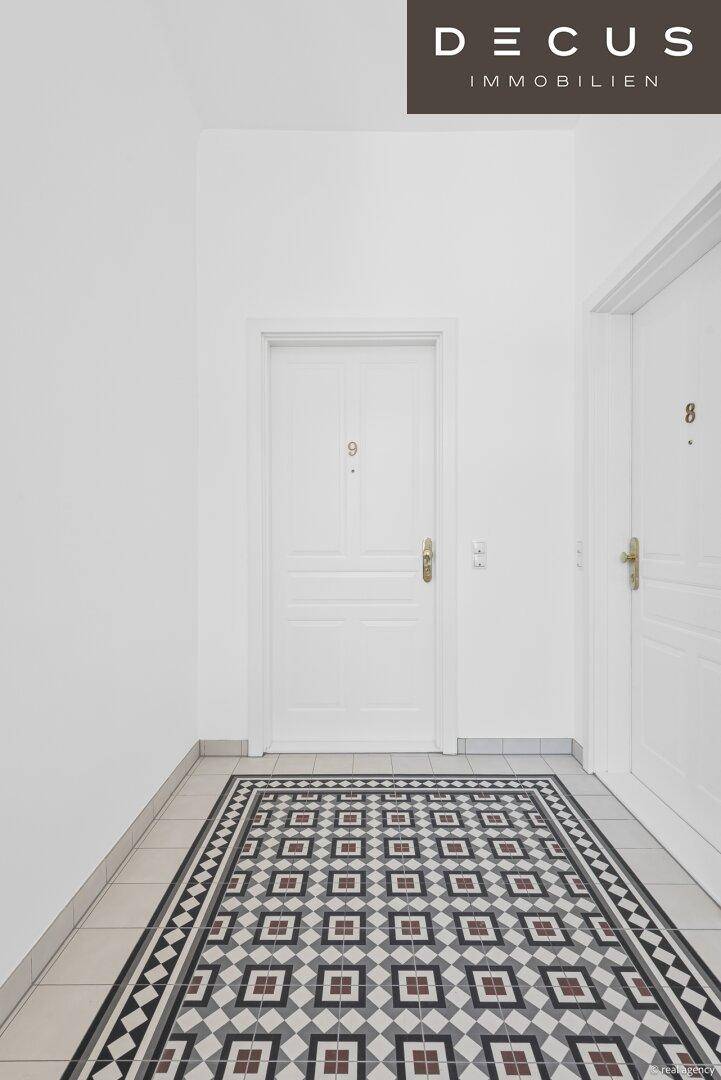 Heller Flur mit auffälligem geometrischem Fliesenboden und weißen Türen.