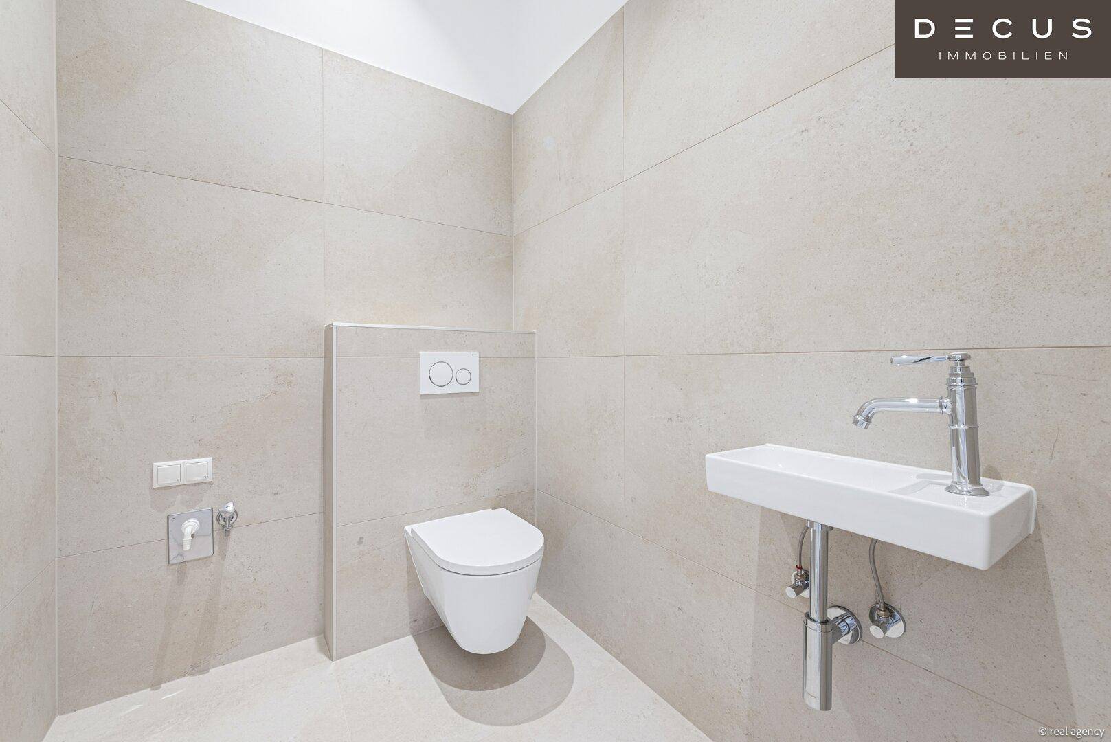 Modernes separates WC mit Wand-WC, kleinem Waschbecken und hellen Fliesen.