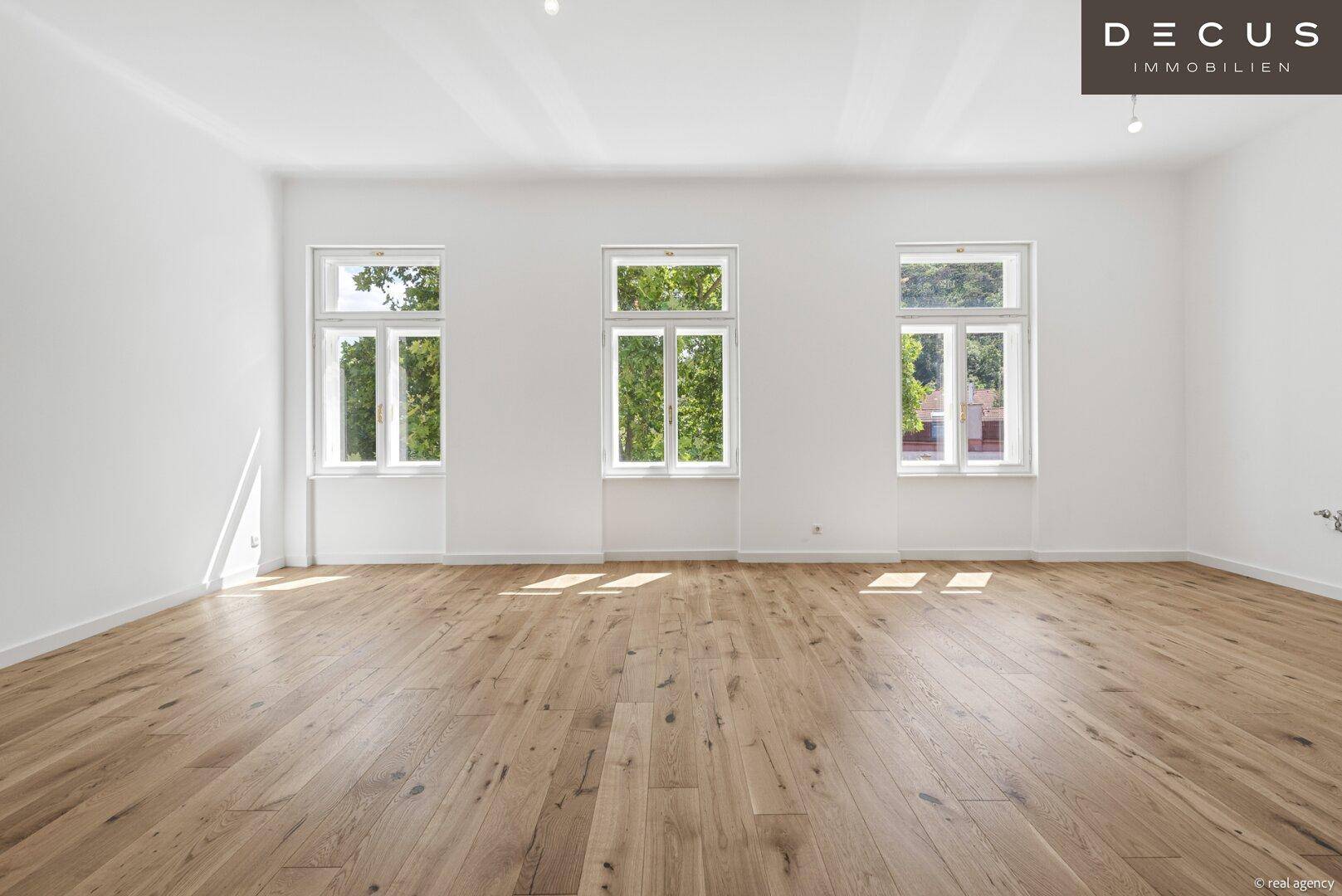 Lichtdurchfluteter Raum mit elegantem Holzboden und hohen Fenstern, die viel Tageslicht hereinlassen.