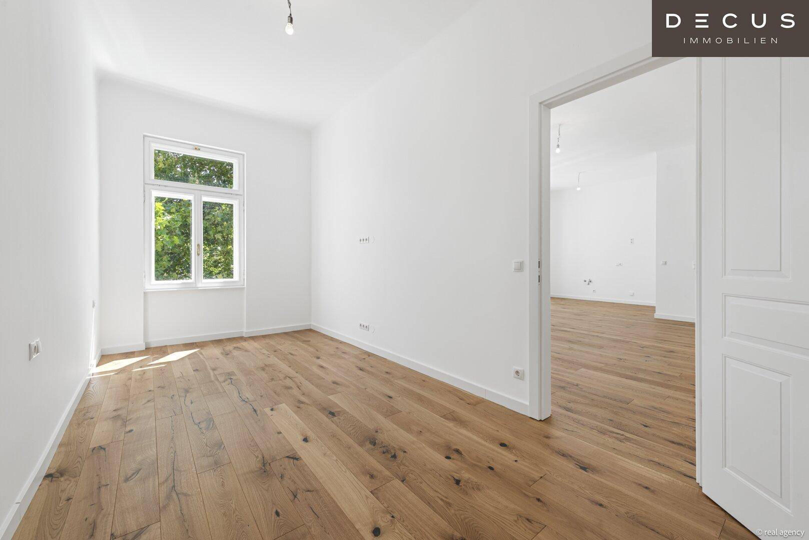 Heller Raum mit Holzdielenboden und Zugang zu einem weiteren Zimmer, ideal als Schlafzimmer.