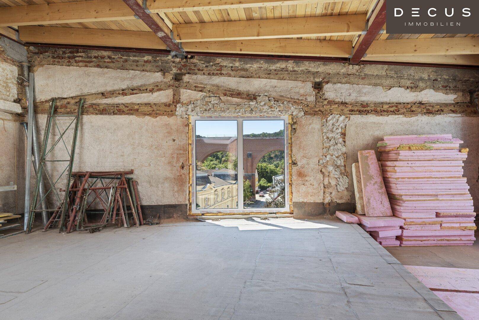 Rohbau mit großer Fensteröffnung, Blick auf eine Brücke und Baumaterialien.