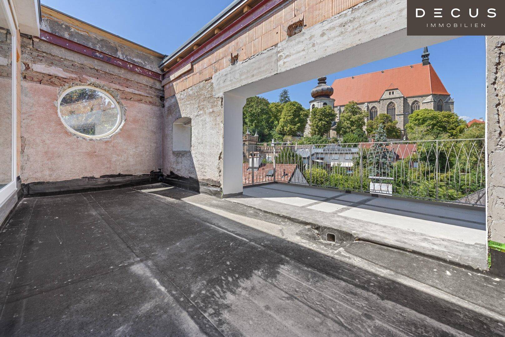Dachterrasse im Rohbau mit Blick auf die Stadt und historische Gebäude.